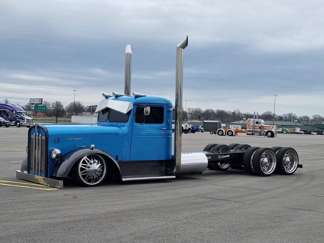 Blue customized semi-truck with lowered suspension and chrome accents in a parking lot.