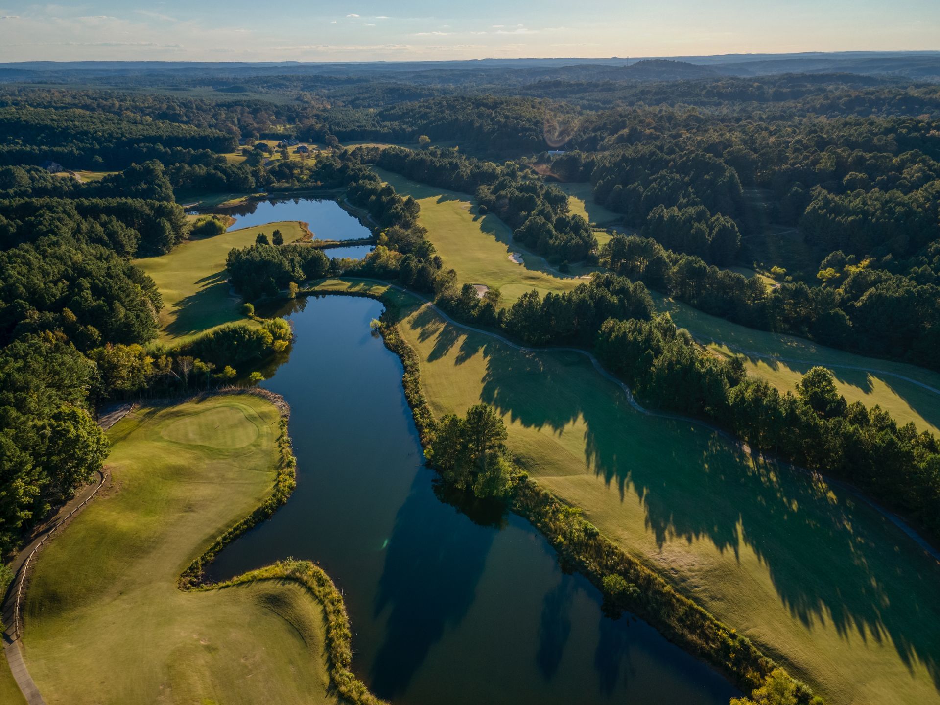An aerial view of a golf course surrounded by trees and a lake.