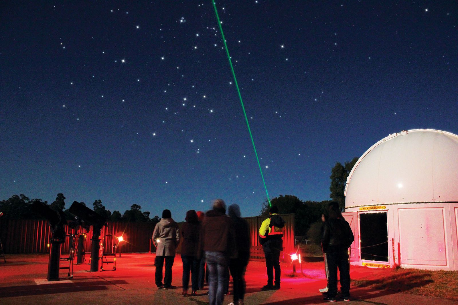 A group of people are standing in front of a dome looking at the stars.