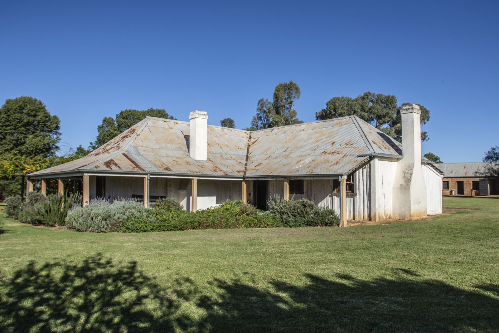 A large white house with a porch is sitting in the middle of a grassy field.