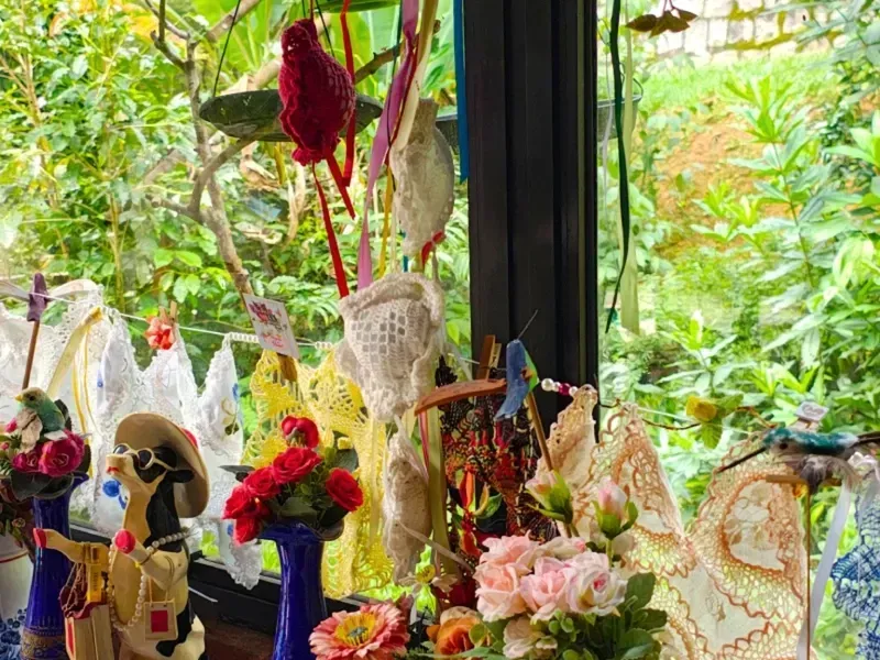 Arranjos florais decorativos e artesanato em uma janela com vegetação exuberante do lado de fora.