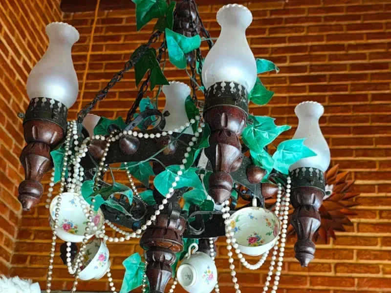 Lustre suspenso ornamentado com cúpulas de vidro fosco branco, madeira escura entalhada e detalhes em folha verde.