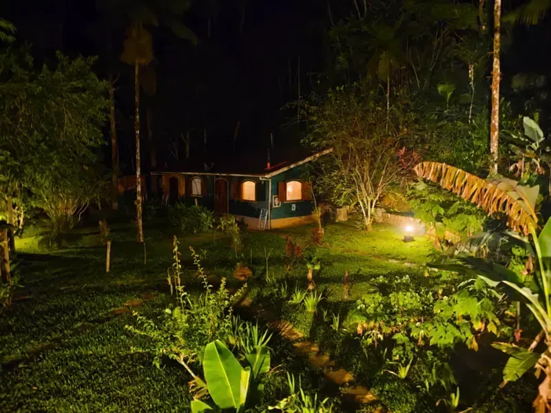 Chalé iluminado à noite em meio a um exuberante jardim tropical e palmeiras.