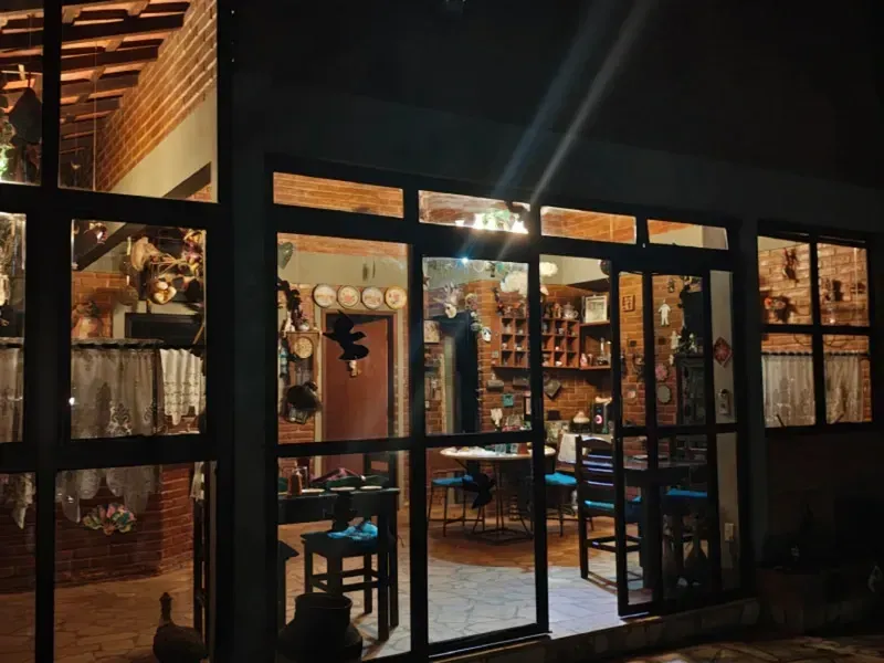 Interior de café com iluminação aconchegante, visto através de portas de vidro à noite.