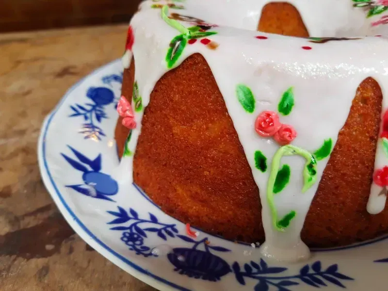 Bolo branco com cobertura de glacê e flores verdes e vermelhas em um prato azul e branco.