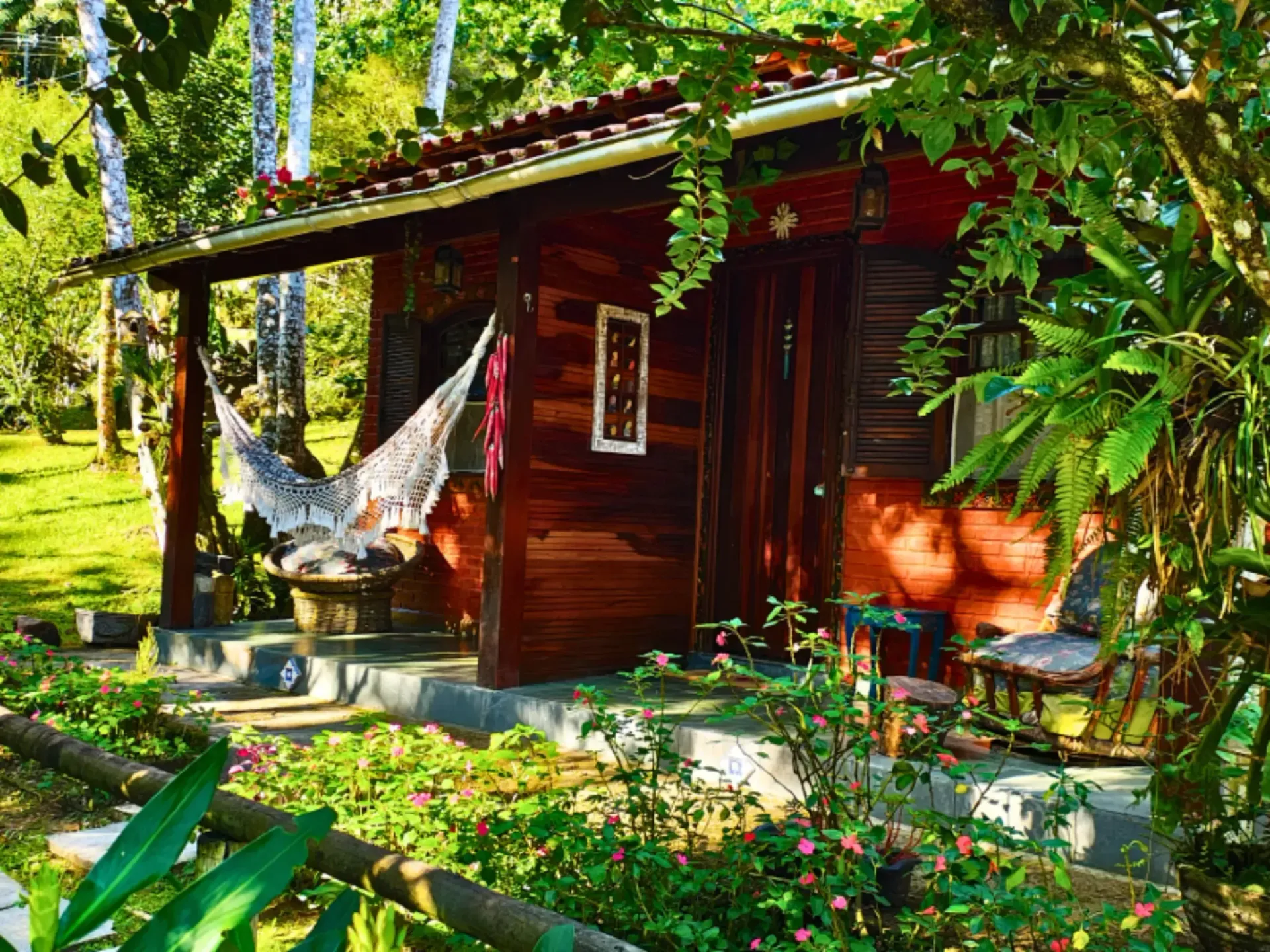 Cabana rústica de madeira com uma rede em uma varanda ensolarada de jardim tropical.
