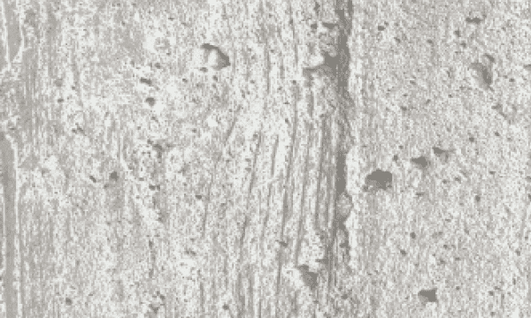 Gros plan sur une surface texturée en béton gris clair, présentant de petits creux et des rainures verticales.