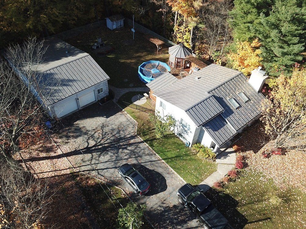 An aerial view of a house and detached garage surrounded by trees, with two cars parked in the driveway.