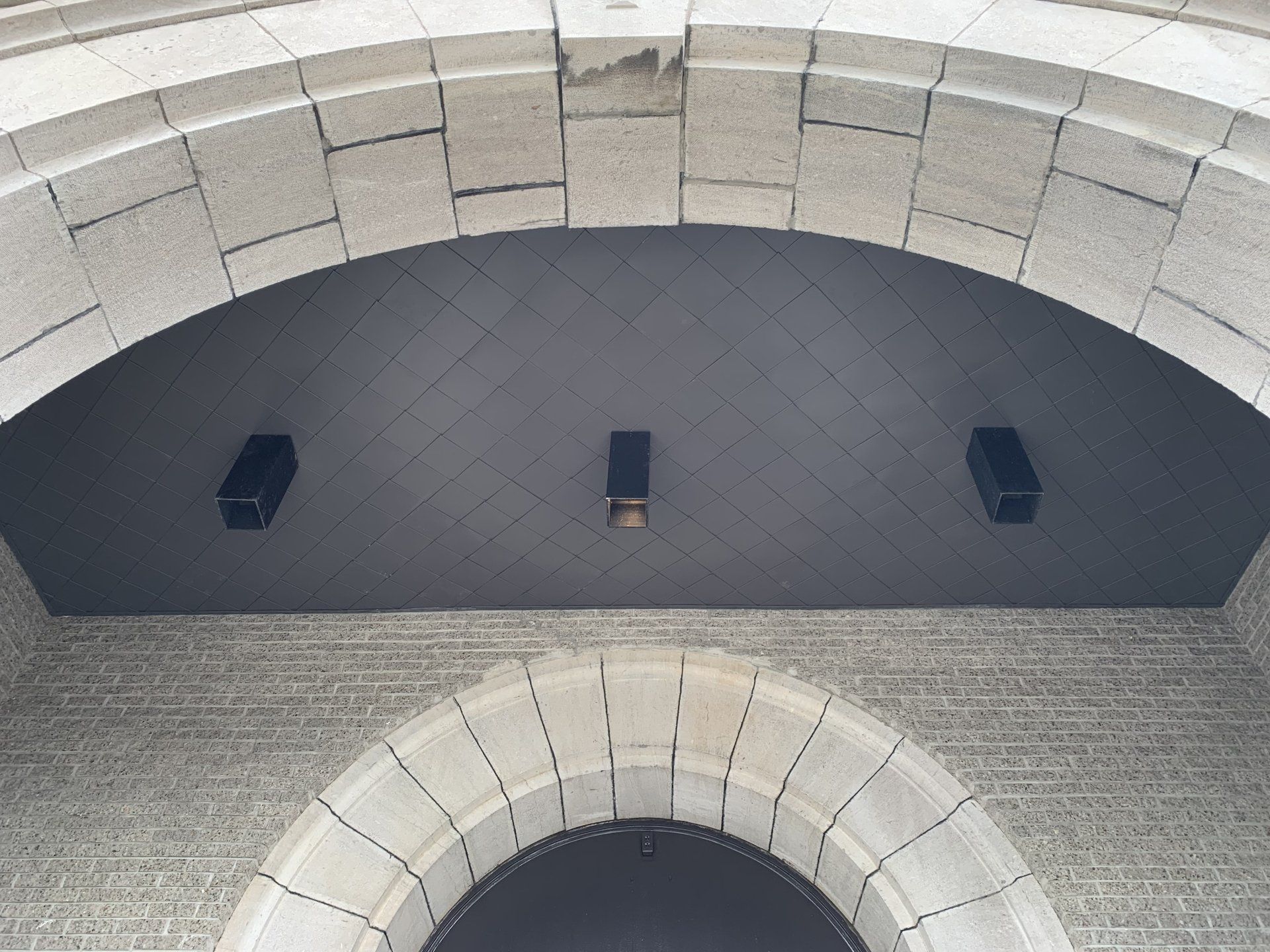 A dark, arched wall feature with three small rectangular lights, framed by decorative, light-colored stone masonry.