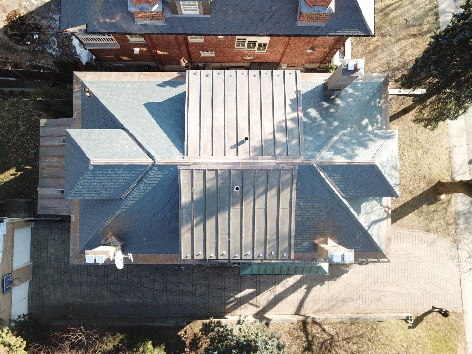 Aerial top-down view of a residential house roof with a mix of shingle and standing seam metal sections.