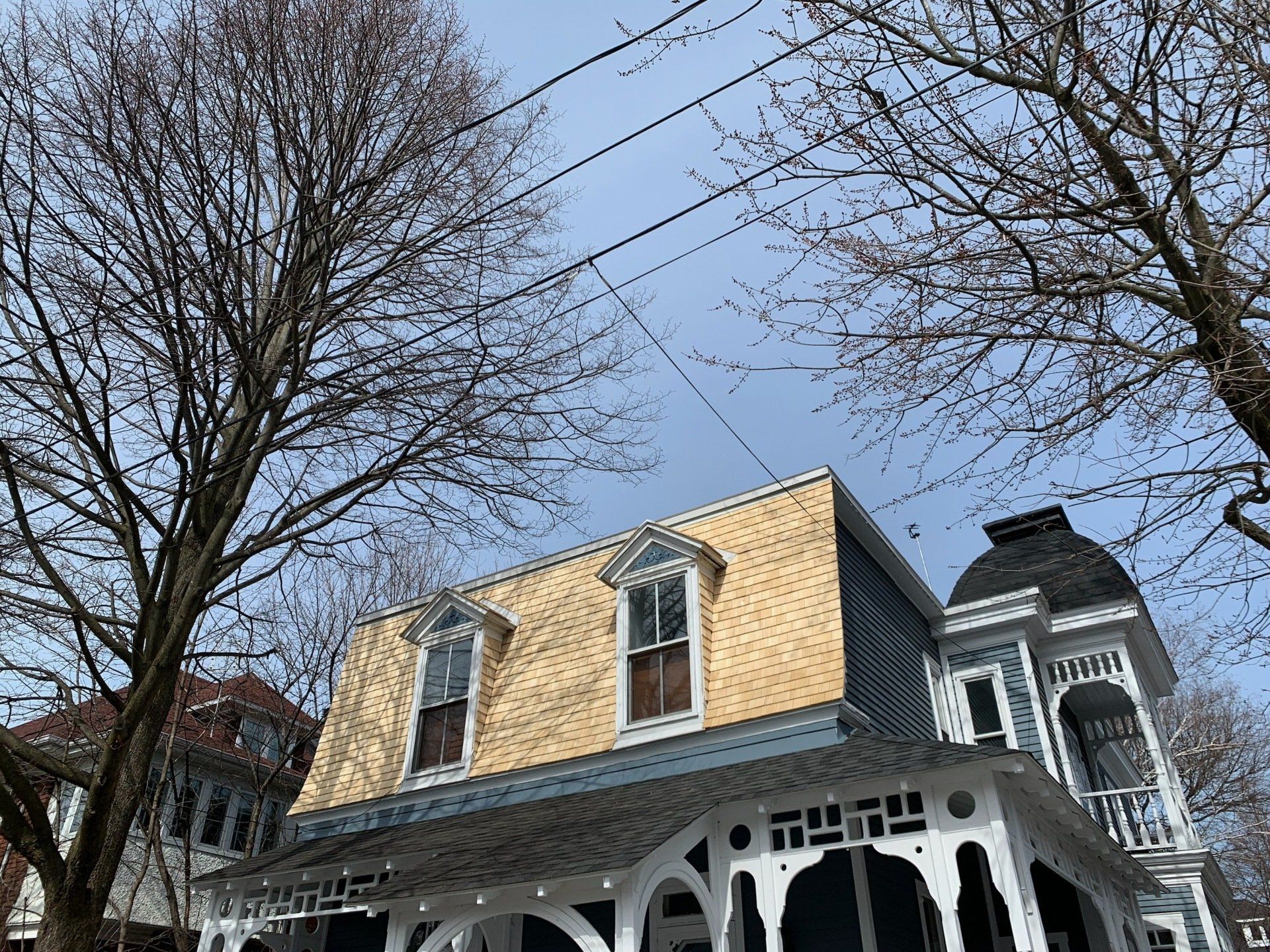 A yellow-walled Victorian-style house with intricate white porch trim, framed by bare trees against a blue sky.