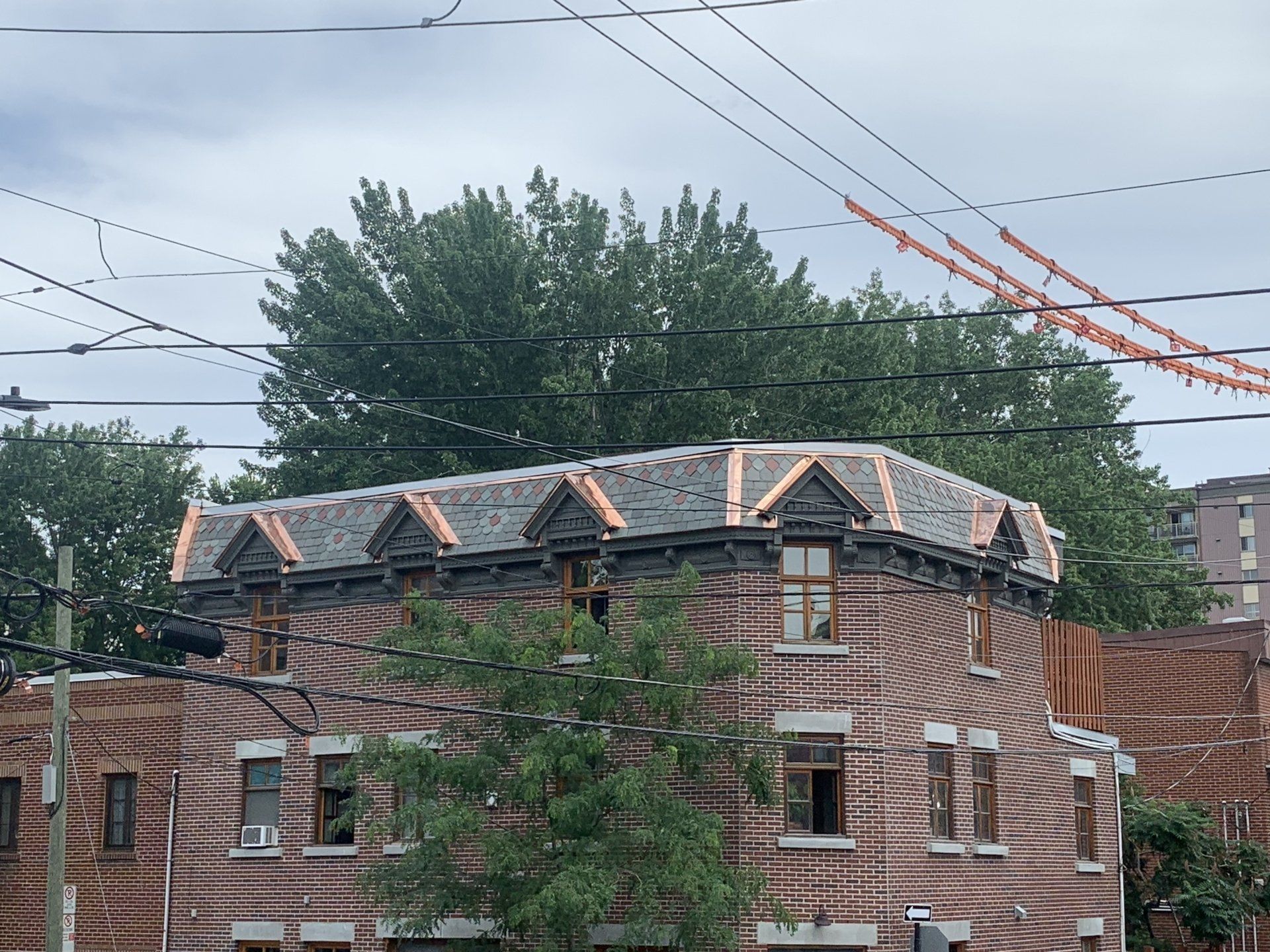 A brick building with a newly installed gray shingled mansard roof featuring small dormer windows and copper flashing.