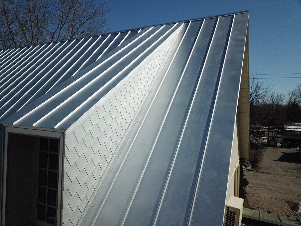 A close-up view of a metal roof with vertical standing seams and a dormer window covered in textured white panels.