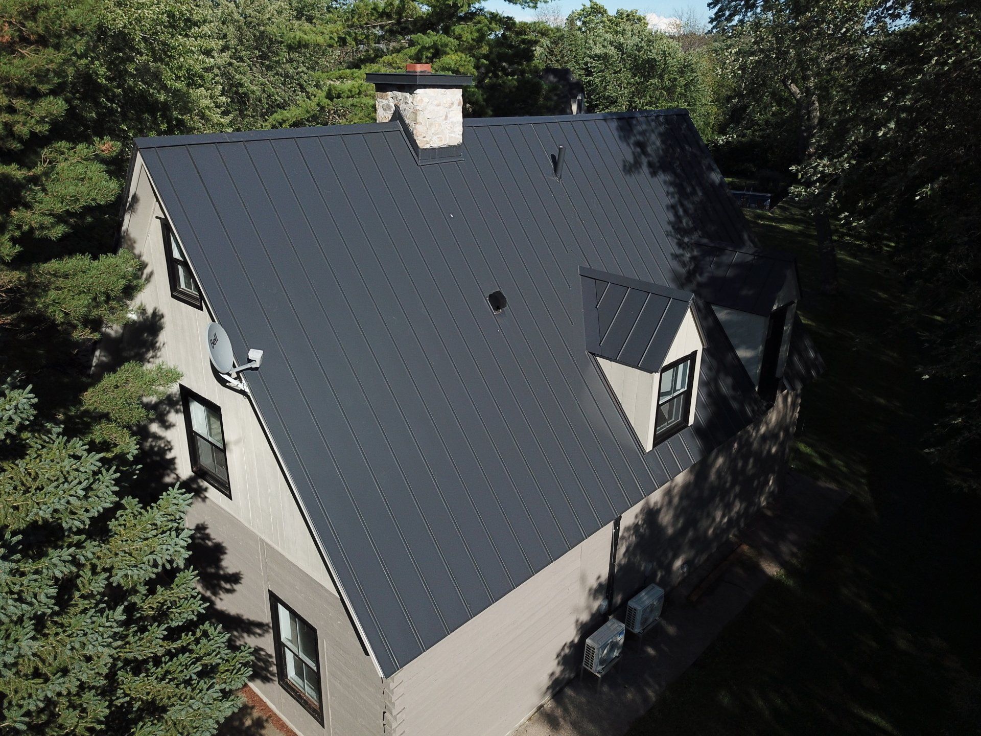 Vue aérienne d'une maison à deux étages avec un toit en métal de couleur sombre, entourée d'arbres.