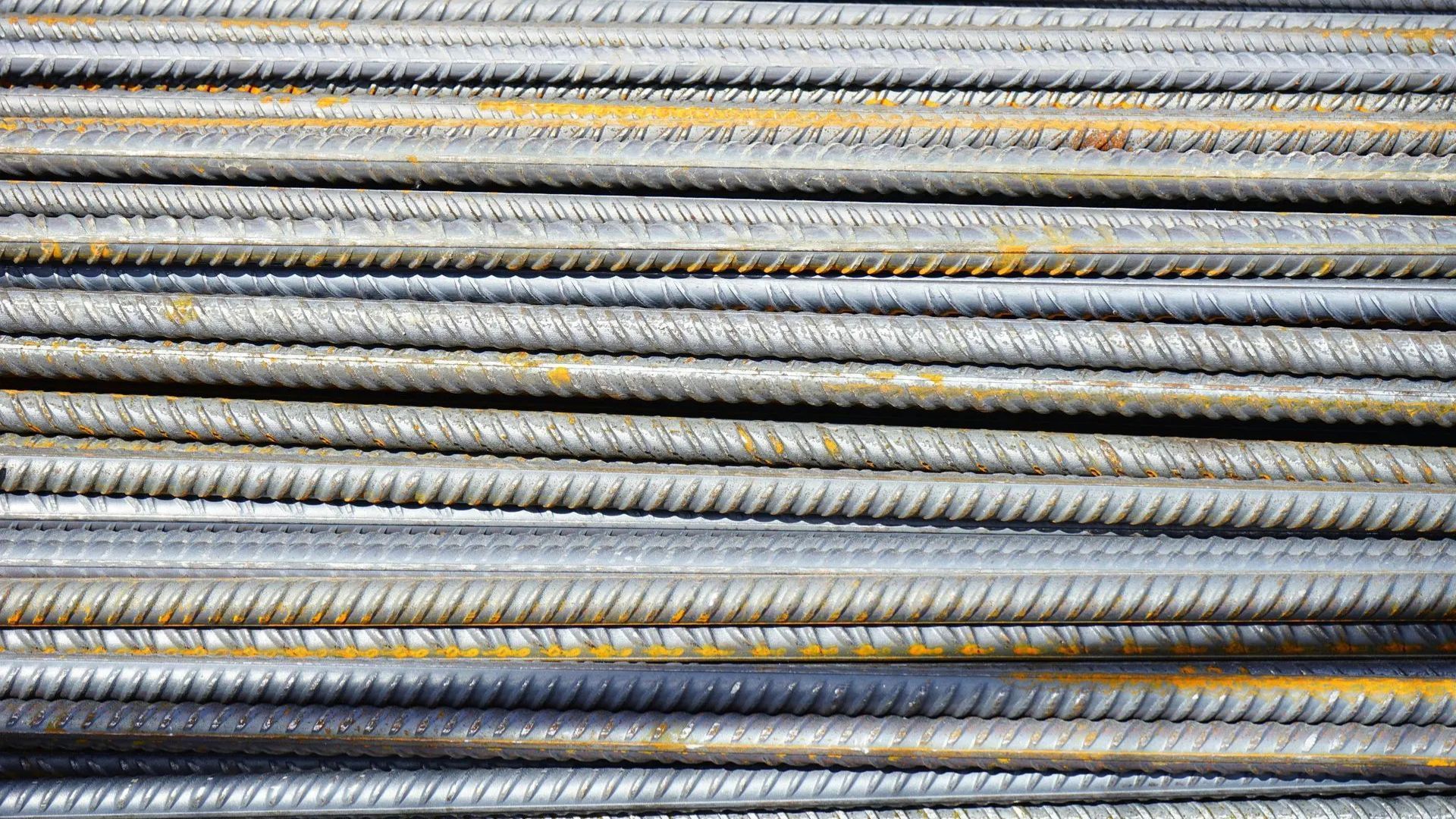 Stacked metal reinforcement bars with ribbed, silver-gray surfaces and yellow markings.