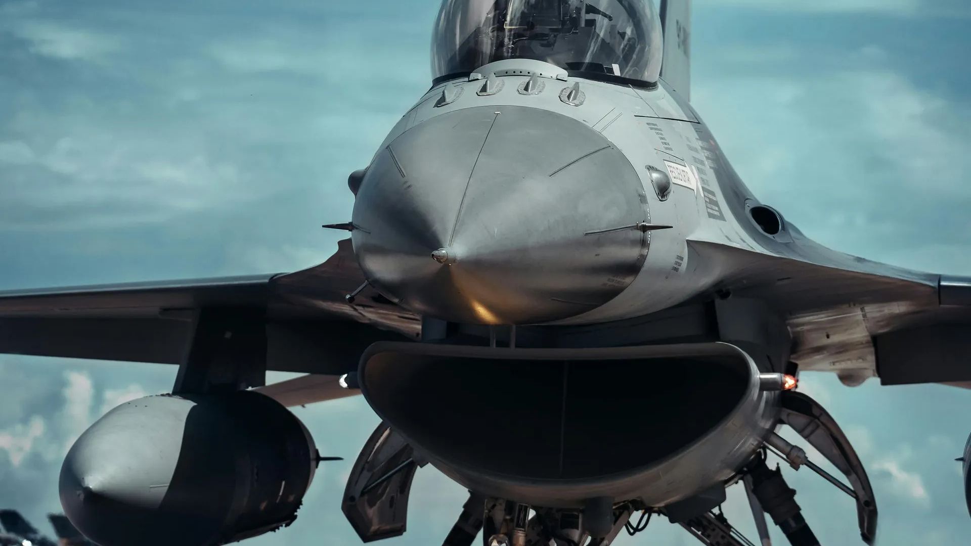 Front view of a gray fighter jet on a runway under a cloudy sky
