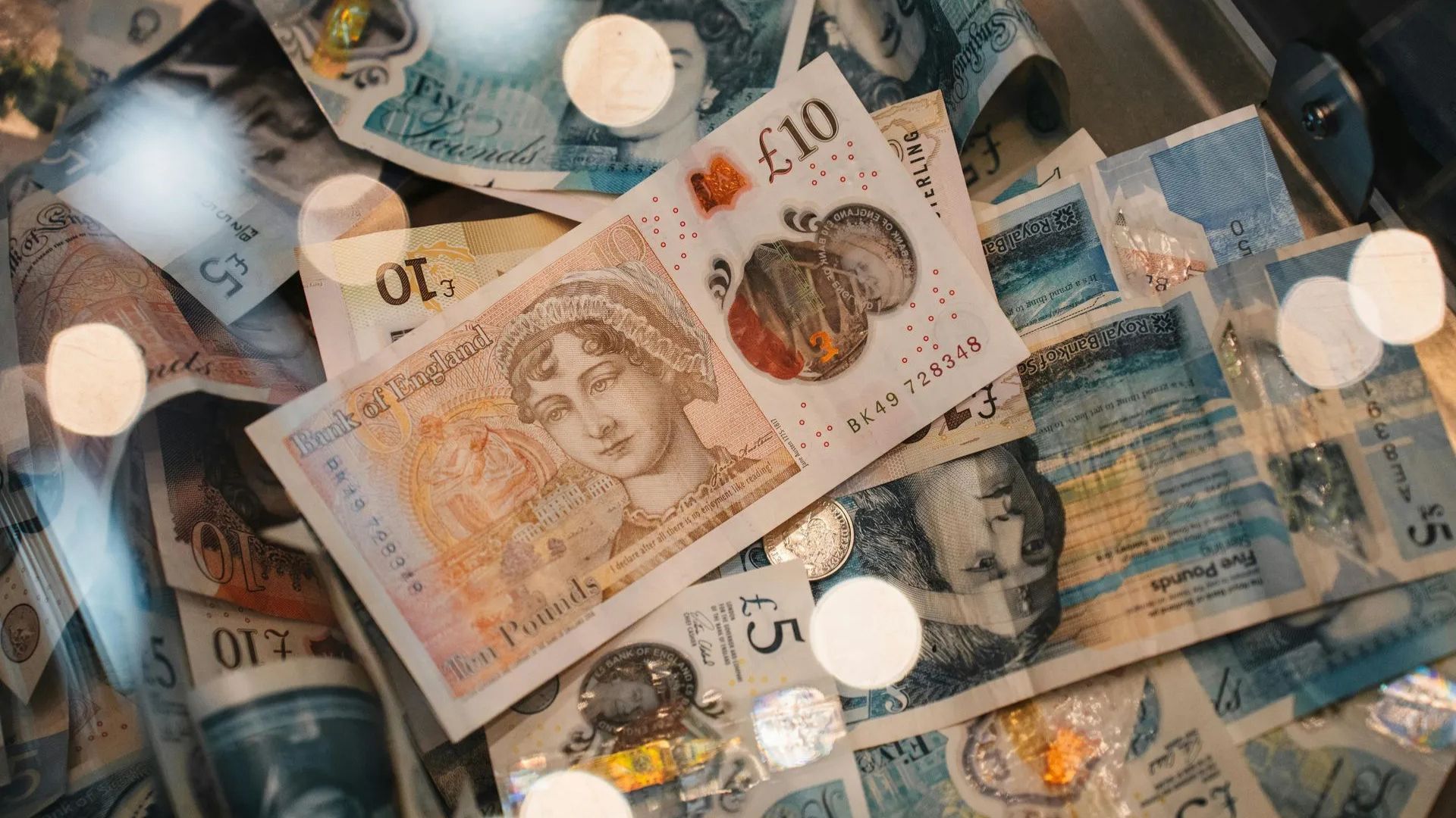 Scattered British pound banknotes in assorted denominations with warm lighting and blurred reflections