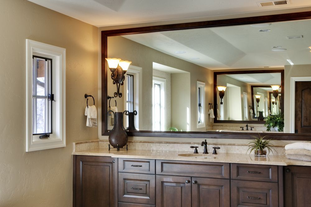 Bathroom With Large Mirror, Dark Wood Vanity, Cream Countertop, Small Window, and Wall Sconces
