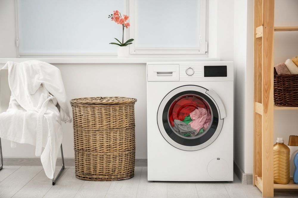 A Washing Machine Is Sitting in A Laundry Room Next to A Wicker Basket — Rodney Lees Cabinetmaking In Lismore, NSW