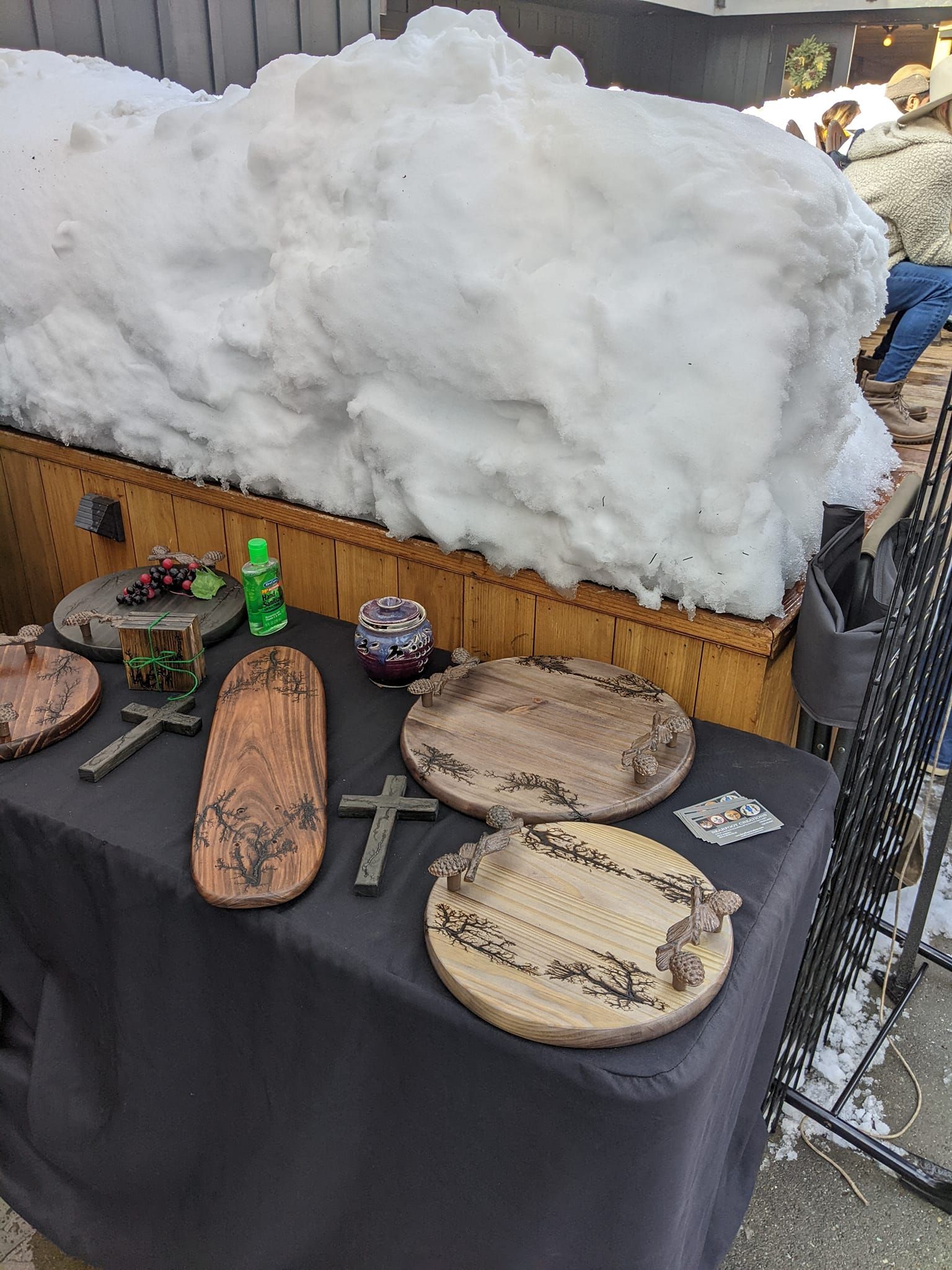 Table with pottery, crosses, and glass objects, with a large snow pile behind it.