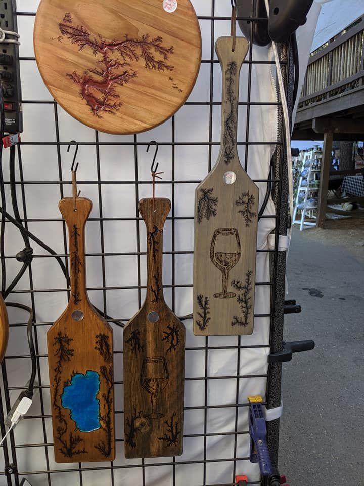 Wooden decorative paddles with burnt designs hanging on a wire grid; one with a wine glass.