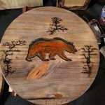Wooden round table with a bear design. The bear is brown, surrounded by trees.