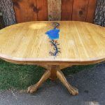 Oval wooden table with a blue resin and black vine design, sitting outside.