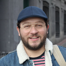 Smiling man in glasses and blue cap wearing a denim jacket with a shearling collar outdoors