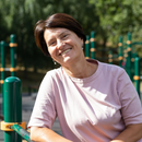 Smiling person in a pale pink shirt outdoors by green playground equipment