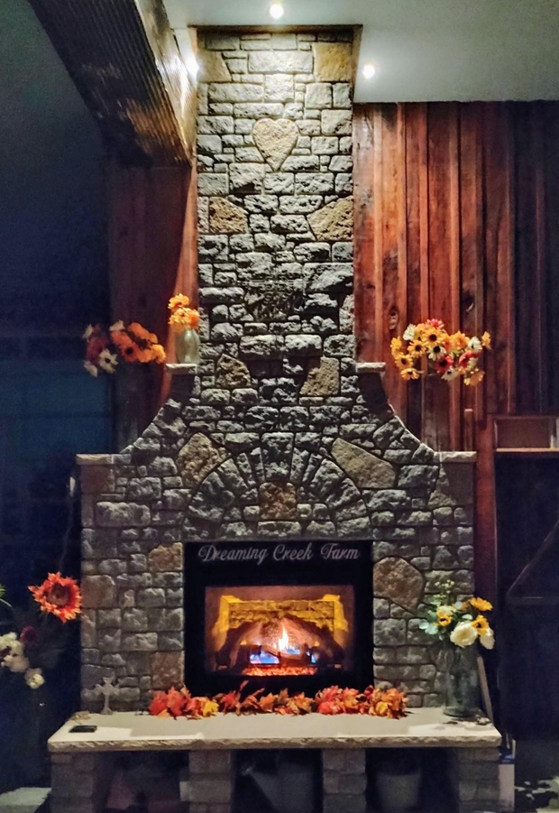 Stone fireplace with a lit fire, autumn leaves, and orange flowers in a cozy room