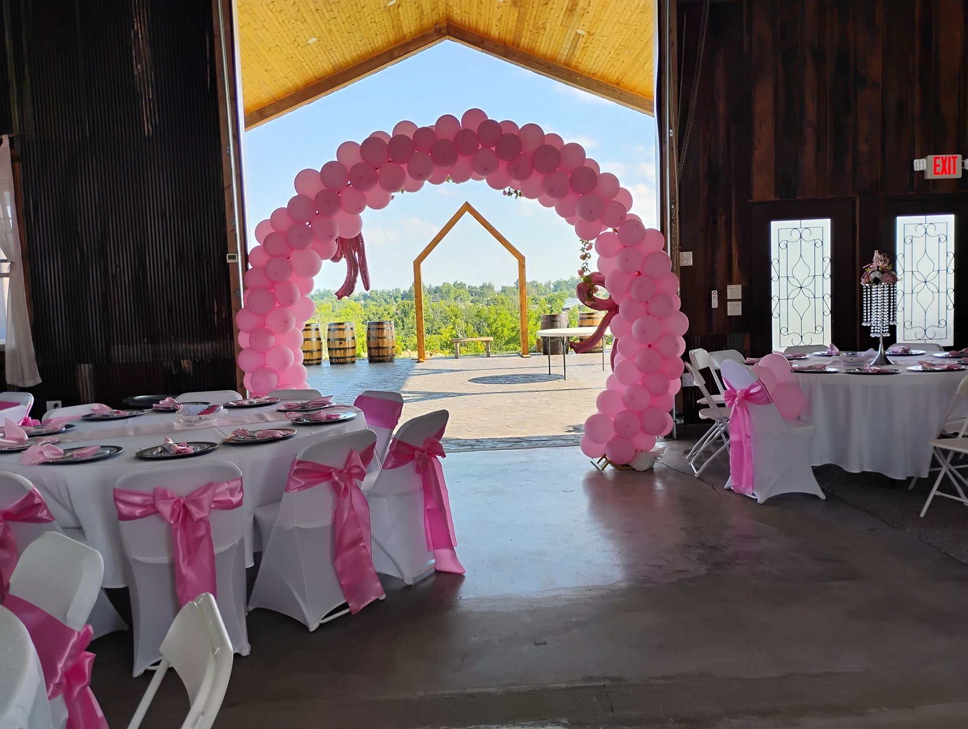 Pink balloon arch in a decorated event hall with round tables and chairs for a celebration