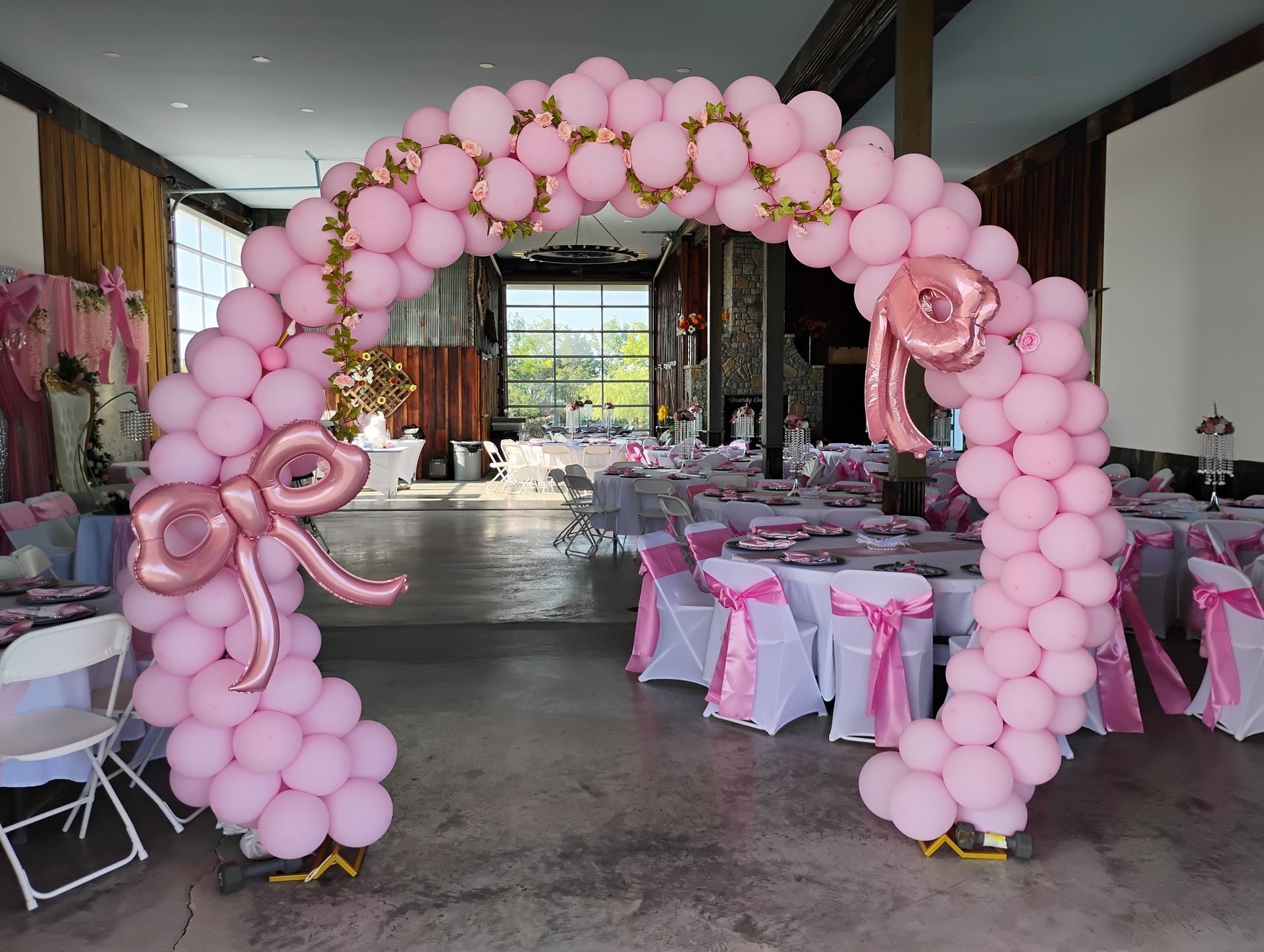 Pink balloon arch decorating a party venue with tables covered in pink chair covers