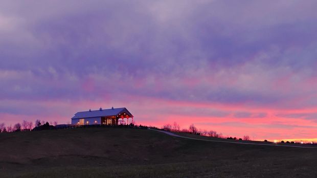 Small house on a dark hill at sunset under a pink and purple sky