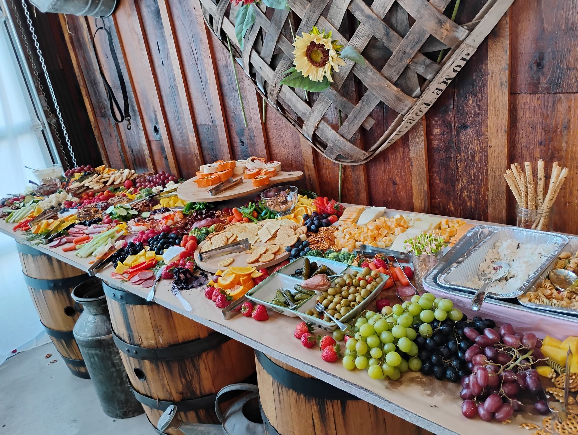 Buffet table with assorted appetizers, fruit, and breads against a rustic wooden wall
