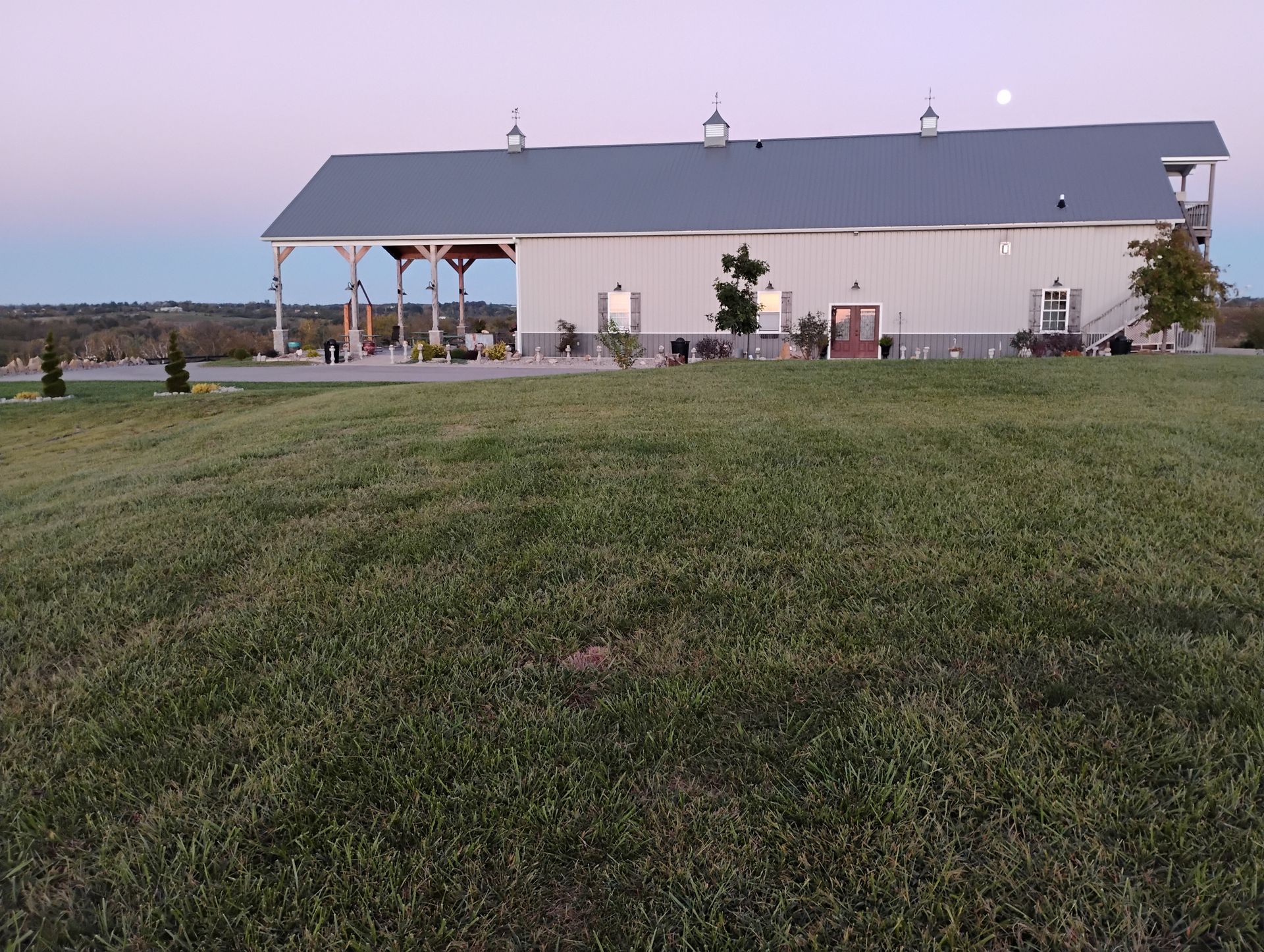 Wide grassy field in front of a small white barn at dusk, with a pink sky behind it.