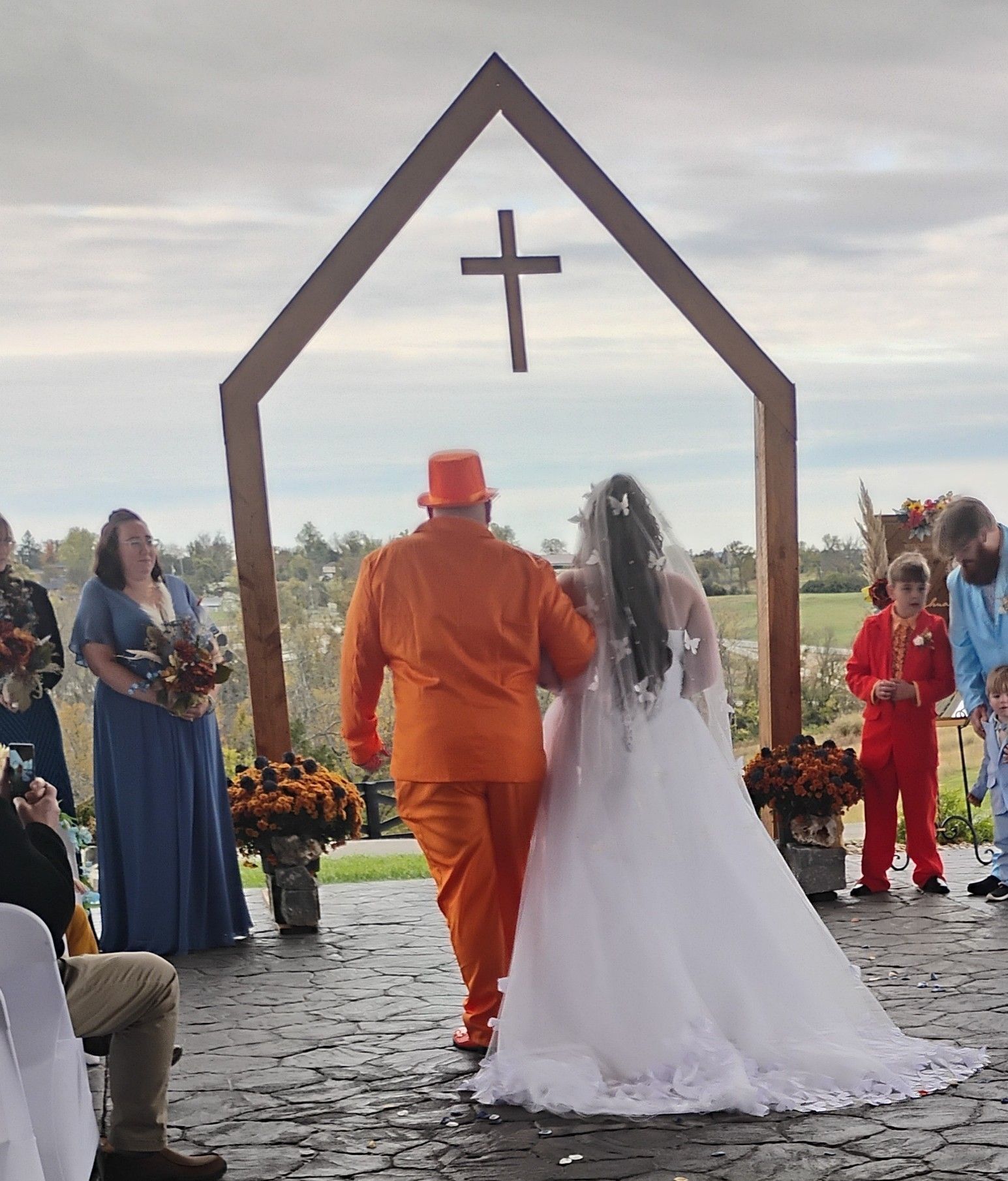 Wedding couple walking under a wooden arch with a cross by a lakeside ceremony