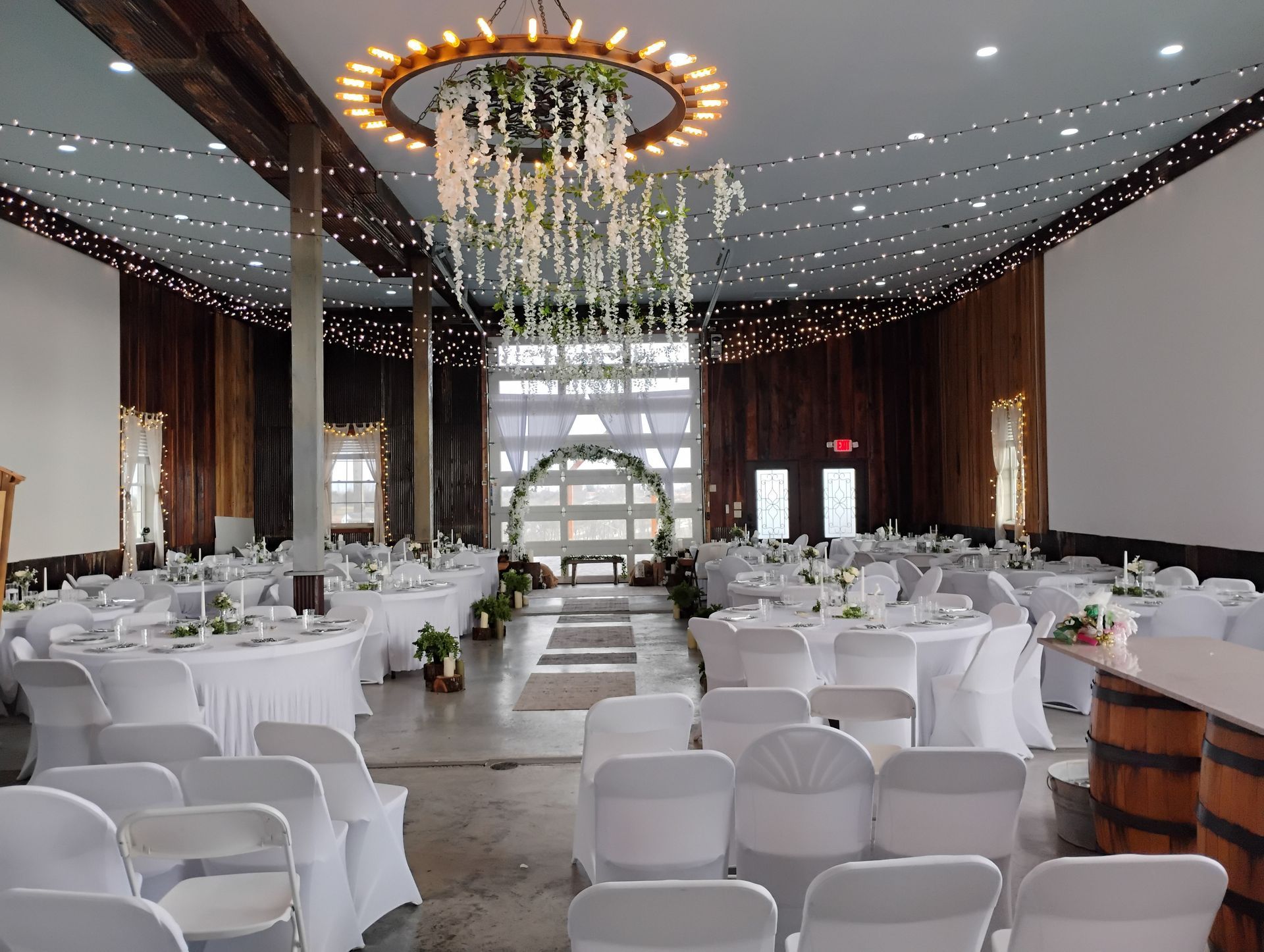 Elegant banquet hall with round white-clothed tables, white chairs, and a large hanging floral chandelier