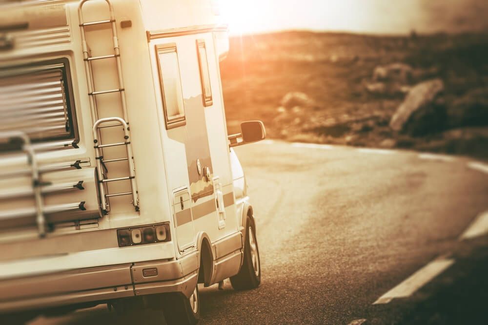 A Camper Van Is Driving Down A Curvy Road At Sunset — Affordable Caravan Repairs in Bundaberg, QLD
