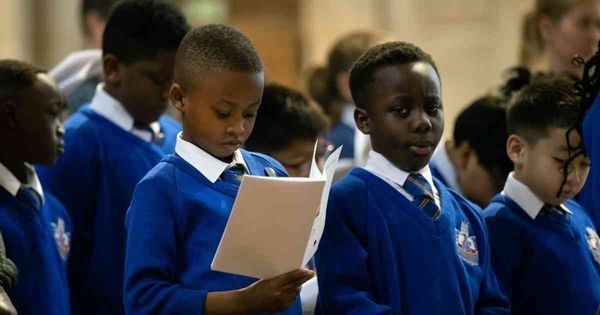 A group of children in blue uniforms are singing in a church.