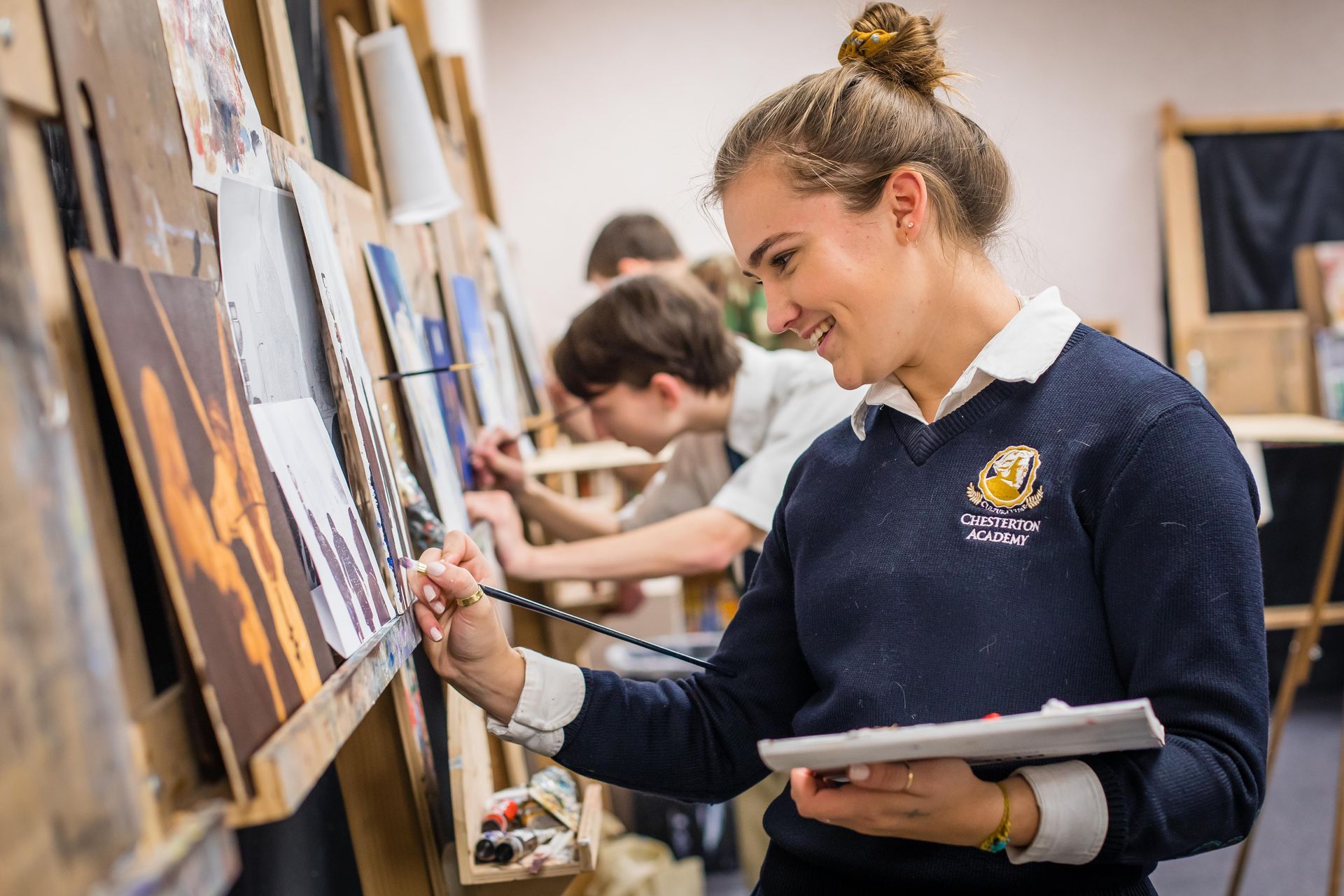 A girl in a blue sweater is painting a picture