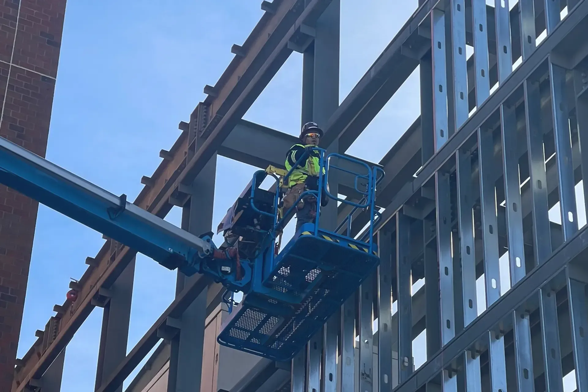 A man is standing on a lift in front of a building under construction.