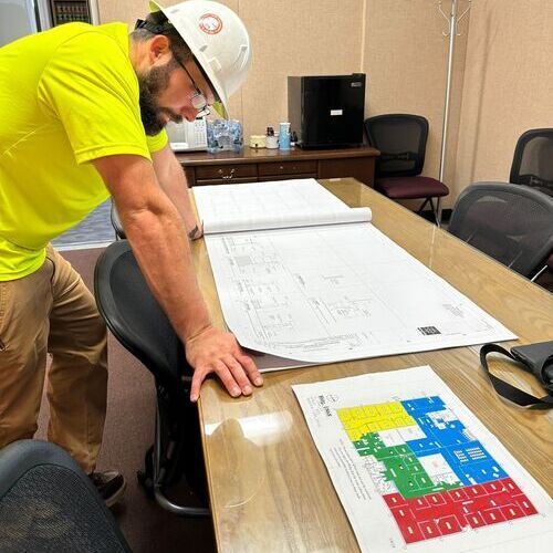 A man wearing a hard hat is looking at a blueprint on a table.