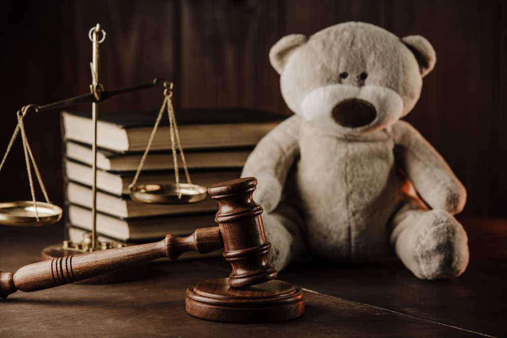 A teddy bear is sitting next to a judge 's gavel and scales of justice.