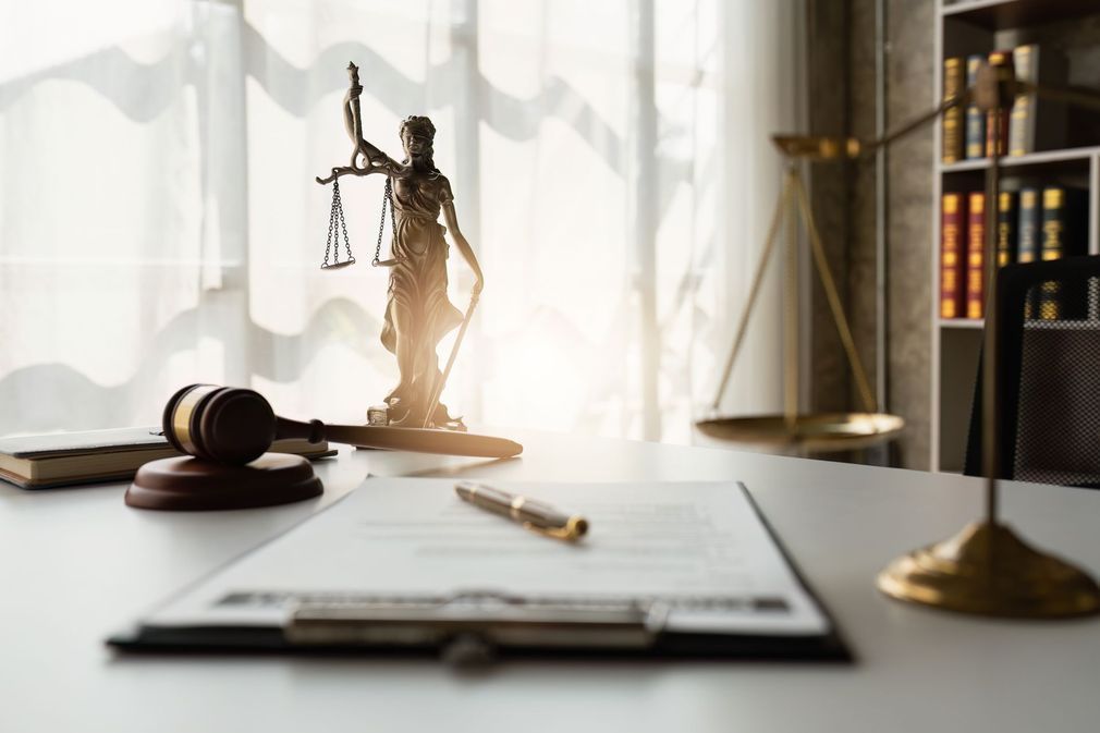 A statue of justice , a gavel , scales of justice , and a clipboard on a table.