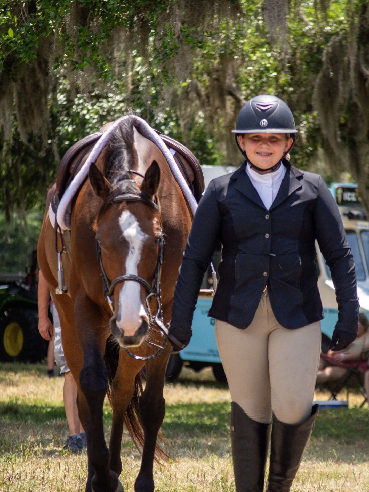 A woman in a helmet is walking a brown horse.