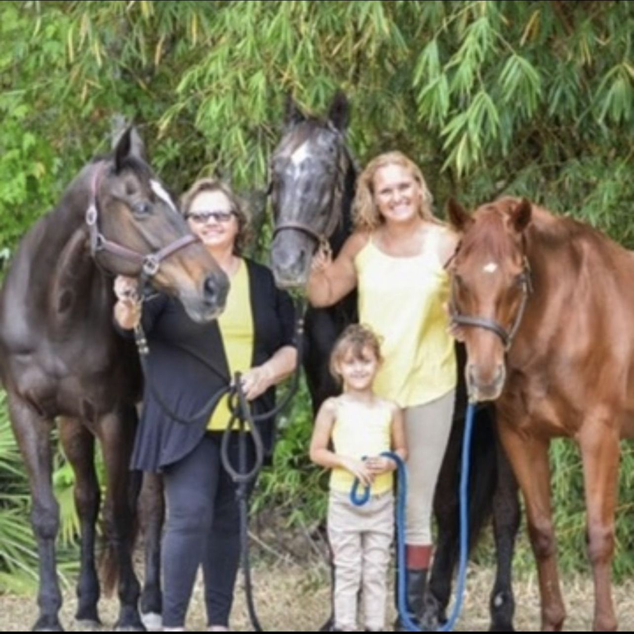 Three women and a little girl are posing for a picture with their horses