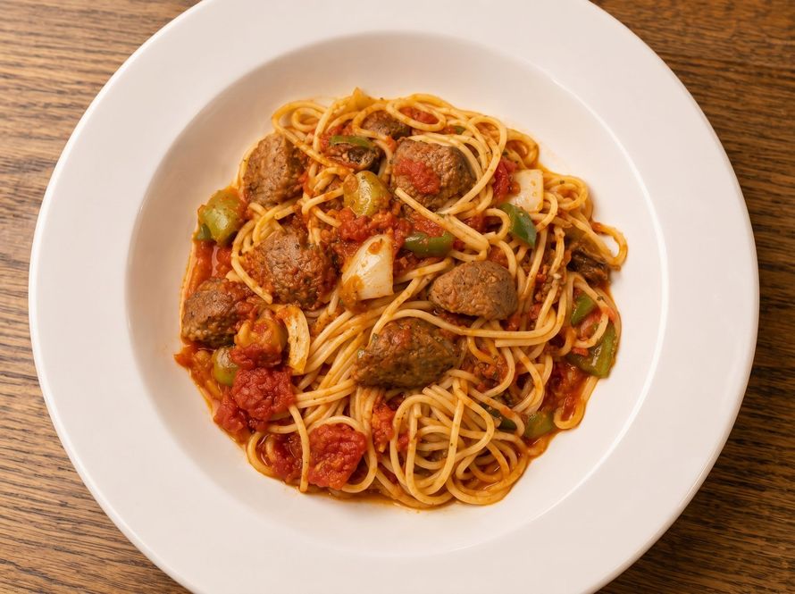 Plate of spaghetti with tomato sauce, meatballs, and green peppers on a white plate
