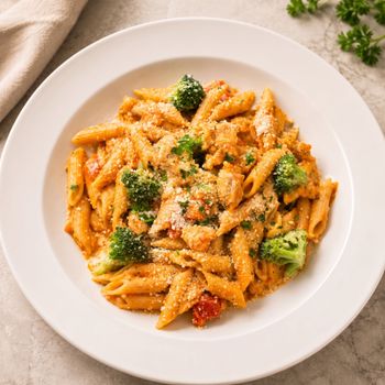 Bowl of penne pasta with broccoli, tomato sauce, and grated cheese on a white plate