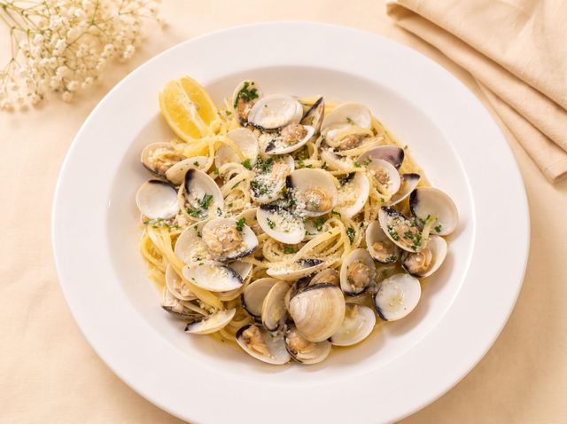 Lemon clam pasta with parsley and grated cheese on a white plate, with wooden utensils beside it