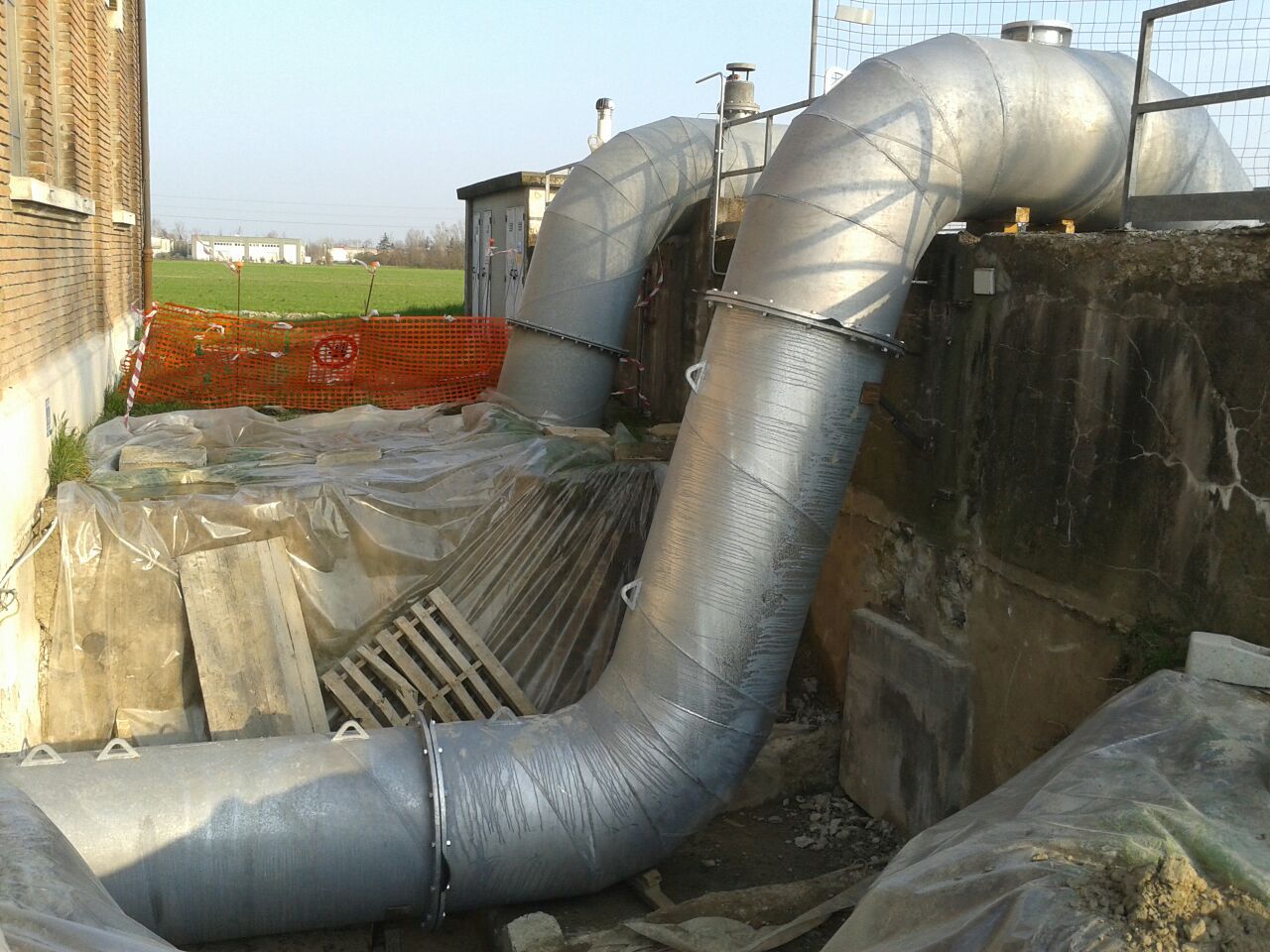 Un grande tubo di metallo è appoggiato nella terra di fronte a un edificio
